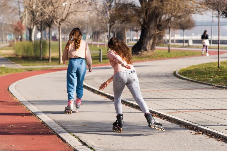 Two young women roller skating in a park on a sunny day.